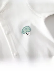 Macro detail of baby romper showing cotton fabric, mushroom embroidery, and resin snaps