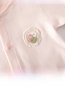 Detailaufnahme rosa Baby-Strampler aus Baumwolle mit feiner Blumenstickerei und Knöpfen