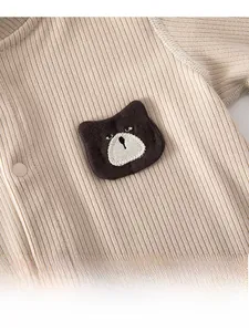 Detail of baby romper featuring a cute brown knitted bear patch on ribbed fabric
