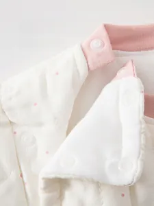 Detail of eco-friendly resin snap buttons on warm beige cotton baby jumpsuit with pink dots