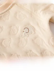 Detailed close-up of warm beige quilted baby romper fabric with 3D elephant jacquard texture