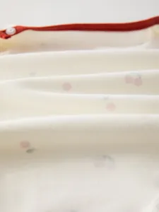 Dettaglio ravvicinato del morbido cotone per body neonato con stampa a ciliegia e bottone bianco