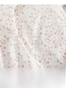 Vue détaillée du barboteuse bébé en coton crème avec imprimé floral rouge et boutons