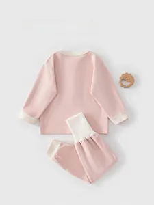 Flat lay of baby pink ribbed cotton pajama set with cream cuffs and wooden lion toy
