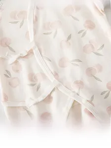 Dettaglio tutina neonato in cotone con stampa di mele rosa e chiusura con fiocchi