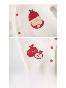 Detail eines Baby-Stramplers mit besticktem Apfel und Bär auf weicher cremefarbener Baumwolle