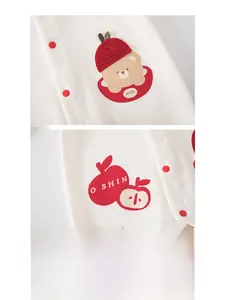 Detail of baby cotton romper featuring embroidered bear and red apple pattern close-up