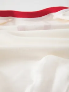 Macro shot of soft cream fine-spun cotton fabric with red trim for baby bodysuit