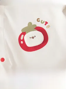 Detail of white baby bodysuit featuring a red tomato patch with CUTE embroidery