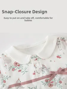 Detail of baby bodysuit featuring unicorn floral print, Peter Pan collar and pink bow accent