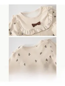 Détail d'un haut bébé en coton avec col en dentelle et nœud décoratif marron foncé