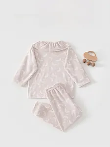 Flat lay of soft pink baby girl cotton pajama set with moon print and wooden toy detail