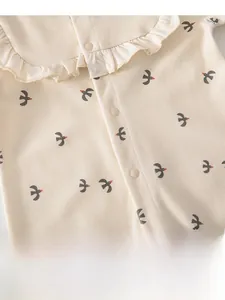 Close-up of baby romper featuring ruffle collar, swallow print, and snap button detail