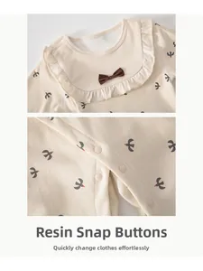Detail of baby romper featuring ruffled collar, brown bow, and resin snap buttons