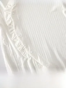Detail of baby bodysuit featuring cream ribbed fabric and ruffled lace edge with snap buttons