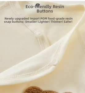 Close-up of baby romper with POM resin snaps and a cute brown plush bear patch detail