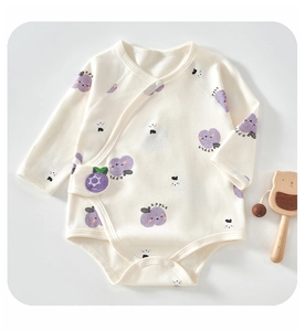Detail of baby cotton romper featuring purple apple print and wooden bear toy