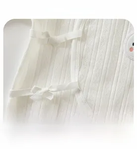 Detail of white cotton baby bodysuit showing jacquard texture and ribbon tie closure