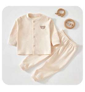 Detailed flat lay of cream cotton baby pajamas set with bear embroidery and wooden toys