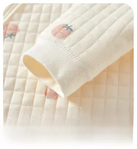 Detailed close-up of soft ribbed cuffs on quilted cotton baby top with peach prints