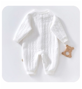 Detail of baby quilted romper showing textured fabric, ribbed cuffs, and wood bear toy