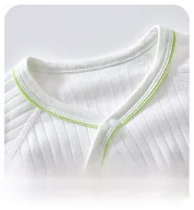 Detail of baby bodysuit bound neckline with green piping and white resin snap button