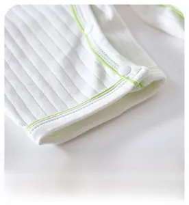 Close-up of white ribbed cotton baby romper featuring green piping and snap button details