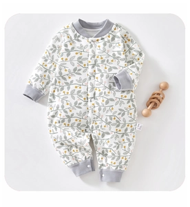 Detail of baby cotton romper featuring natural berry leaf print and wood rattle decor