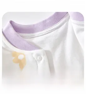Detail of infant bodysuit showing white cotton fabric with purple rib neck and yellow snap buttons