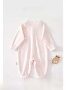 Flat lay of soft pink long-sleeve cotton baby romper with decorative wooden teether