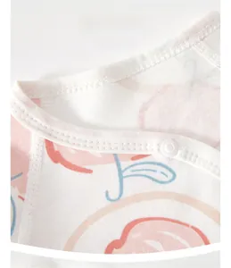 Detail eines weichen Baumwoll-Baby-Stramplers mit Pfirsichdruck und Druckknöpfen