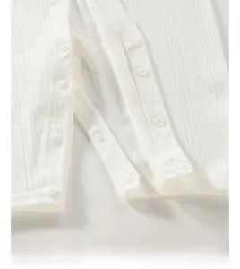 Detail of soft white knit baby romper featuring breathable pointelle patterns and snaps