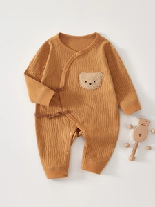Detail of orange waffle knit baby romper with side ties and cute plush bear patch