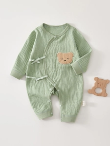 Detail of baby organic cotton romper featuring a cute brown bear patch and soft waffle texture