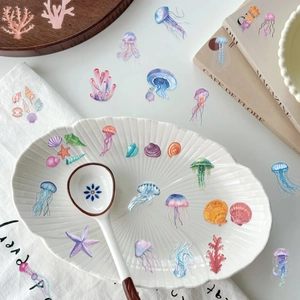 Detailed view of marine PET stickers with jellyfish and shells on a white ceramic plate