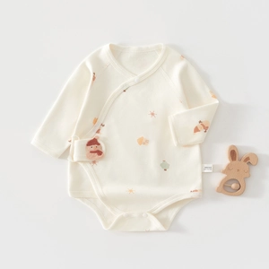 Flat lay of cream cotton baby bodysuit with snowmen prints and wooden rabbit rattle toy