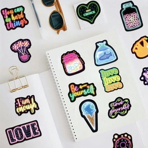Lot de 50 stickers style néon avec phrases inspirantes et icônes sur bureau blanc