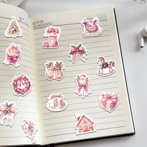 Pink watercolor Christmas stickers on an open notebook showcasing various festive patterns