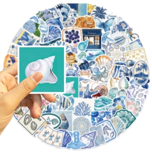 Gros plan d'une main tenant un autocollant aquarelle de coquillage sur fond bleu océan