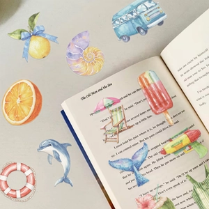 Close-up of watercolor summer stickers on an open book featuring fruit and sea elements