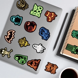 Neon Halloween stickers with ghosts and pumpkins on a silver laptop surface