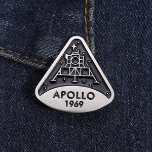 Detail of Apollo 1969 moon landing enamel pin on blue denim fabric with silver lettering