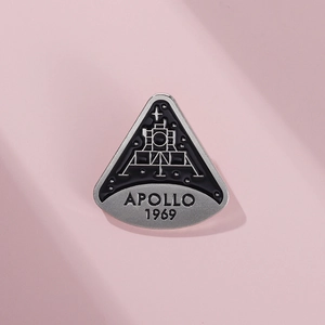 Macro detail of silver Apollo 1969 enamel pin with black drip oil finish and fine engraving
