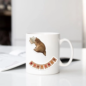 Detail of a white ceramic mug featuring a cute orange cat reading a book illustration