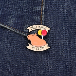 Close-up of enamel capybara pin with balloons pinned on blue denim fabric background