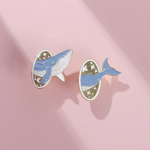 Détail des broches en émail baleine bleue et lune avec bord doré sur fond rose poudré