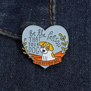 Detail of a heart-shaped enamel pin with dog illustration on blue denim fabric