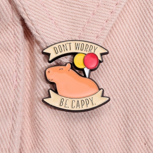 Close-up of orange capybara enamel pin with balloons and Don't Worry Be Cappy text