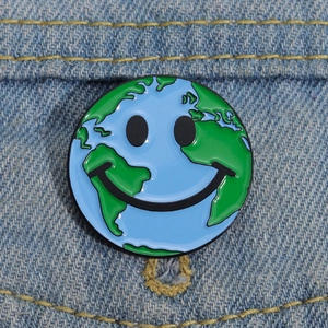 Détail d'un pin's émaillé terre souriante fixé sur un tissu en denim bleu classique