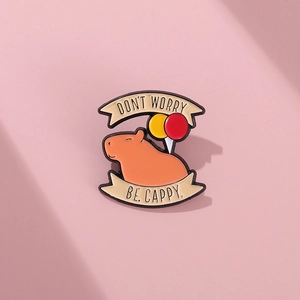 Detail of an enamel capybara pin with balloons and a funny Be Cappy slogan